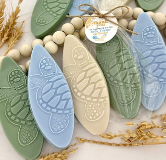 Surfboard-shaped soaps in various colors with turtle patterns, packaged individually with a tag attached.